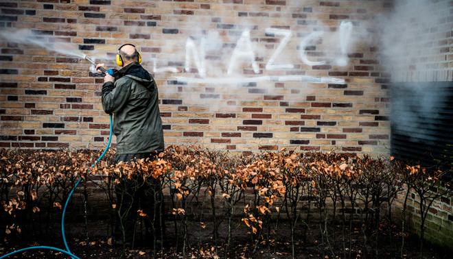 De woorden 'geen azc' worden verwijderd van een muur bij het gemeentehuis in Geldermalsen waar protesten waren tegen een mogelijke azc voor zo'n 1500 vluchtelingen. Foto: Robin Utrecht / Hollandse Hoogte