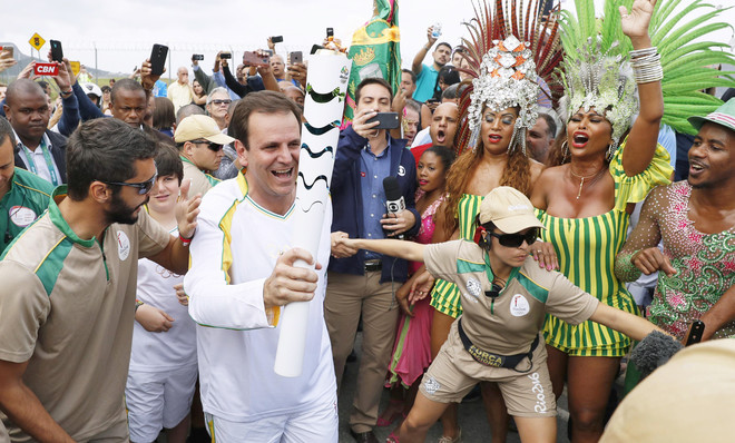 De burgemeester van Rio de Janeiro draagt het Olympisch vuur naar het Maracanã-stadion. Betogers hebben geprobeerd met een plens water het vuur te doven uit protest tegen de miljarden die Brazilië besteedde aan de Olympische Spelen. Foto: Getty
