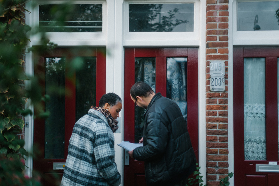 Twee medewerken van Doras (een organisatie voor maatschappelijke dienstverlening in Amsterdam-Noord) gaan de deuren af van mensen met schulden. Uit de serie ‘Schuldig.’ Foto: Jean Counet