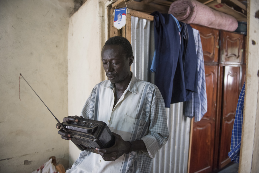 Thomas Ali luistert naar de radio om op de hoogte te blijven van het internationale nieuws. Juba, Zuid-Soedan. Foto: Charles Lomodong (voor De Correspondent)